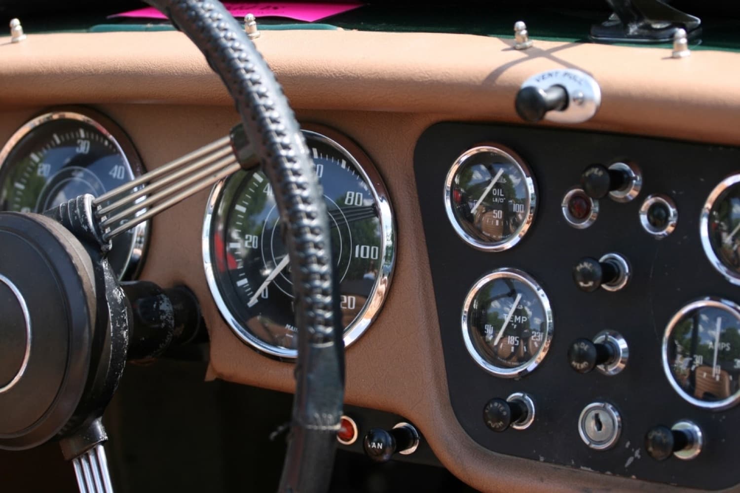 Close-up of a classic car's wood-rim steering wheel and chrome gauges